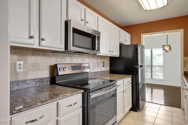 kitchen featuring light hardwood / wood-style flooring, appliances with stainless steel finishes, decorative backsplash, white cabinetry, and dark stone countertops