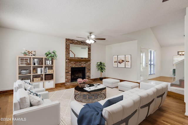 living room with light hardwood / wood-style flooring, vaulted ceiling, a brick fireplace, ceiling fan, and a textured ceiling