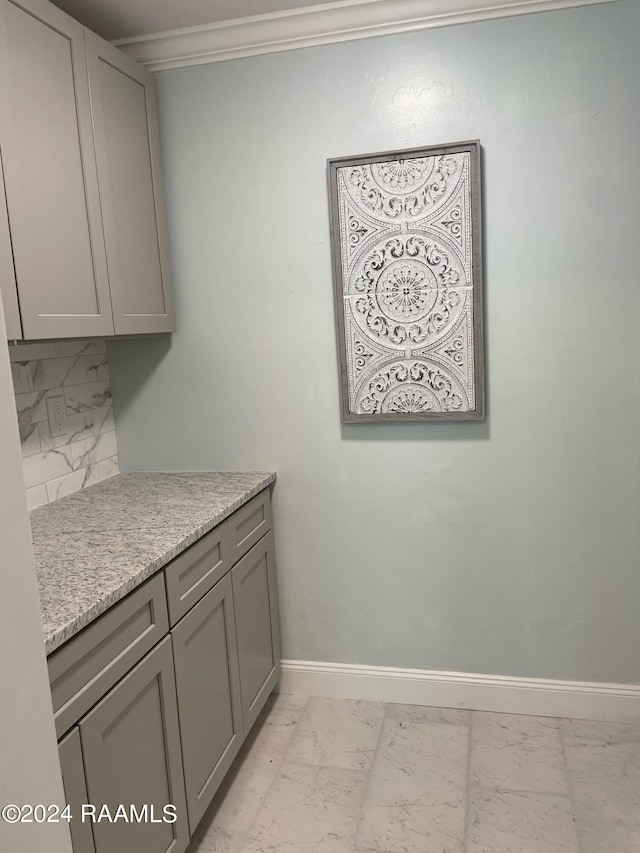 kitchen featuring decorative backsplash, light stone counters, crown molding, light tile patterned floors, and gray cabinets