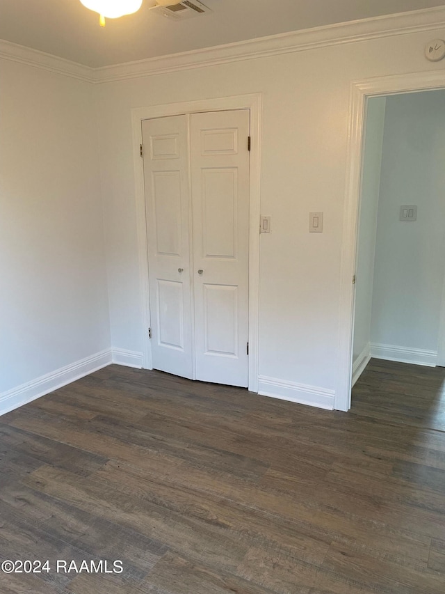 unfurnished bedroom featuring a closet, dark wood-type flooring, and ornamental molding