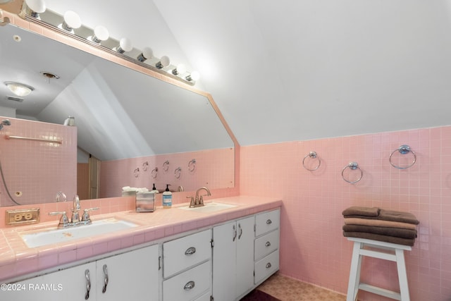full bath with tile walls, double vanity, a sink, and vaulted ceiling