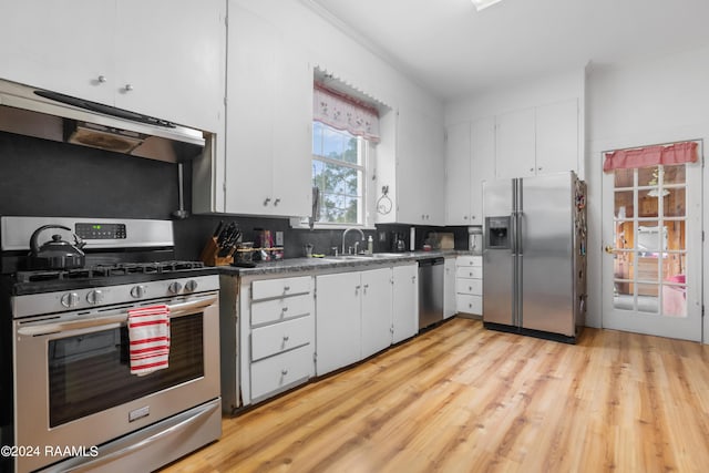 kitchen featuring white cabinetry, under cabinet range hood, a sink, light wood-style flooring, and appliances with stainless steel finishes
