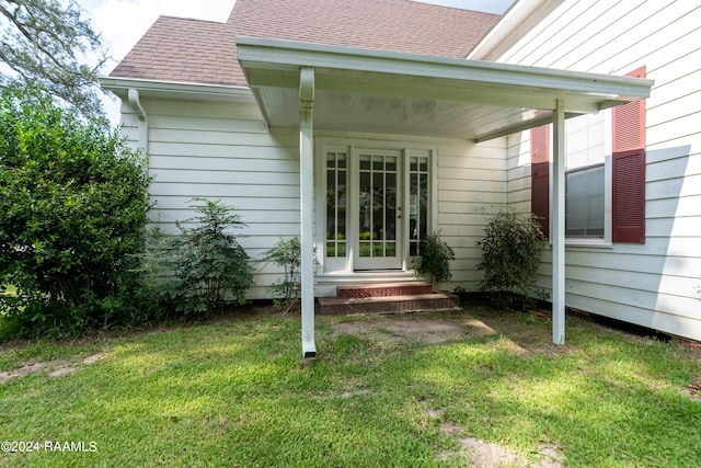 view of exterior entry featuring a shingled roof and a yard