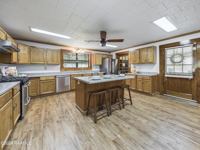 kitchen with under cabinet range hood, stainless steel appliances, a kitchen breakfast bar, brown cabinets, and light wood finished floors