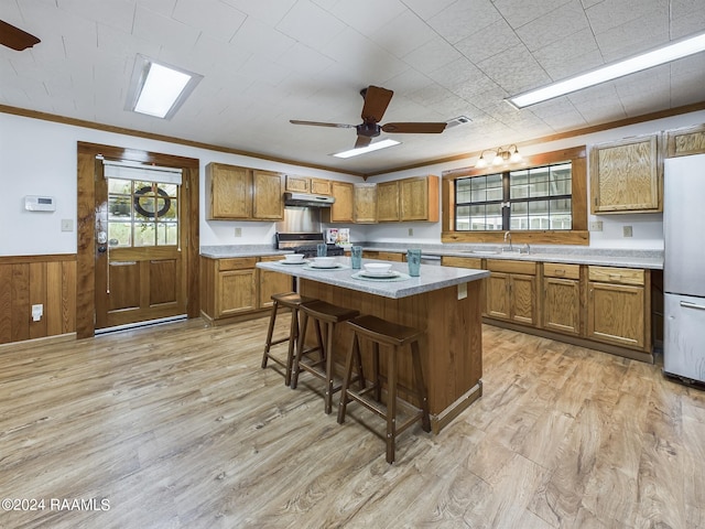 kitchen with under cabinet range hood, wainscoting, brown cabinetry, and freestanding refrigerator