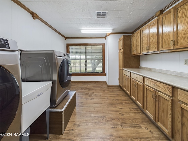 clothes washing area with crown molding, cabinet space, visible vents, a sink, and wood finished floors