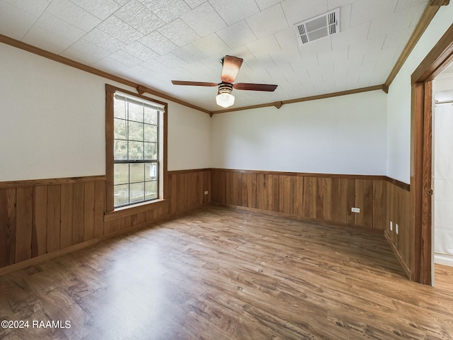 unfurnished room featuring wainscoting, wood finished floors, visible vents, and crown molding