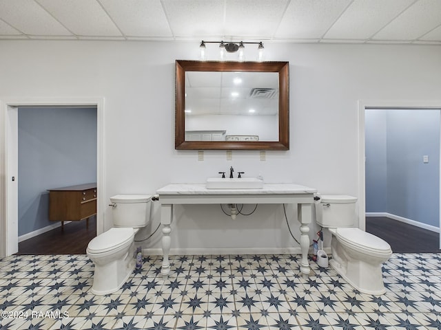 bathroom featuring a drop ceiling, toilet, a sink, visible vents, and baseboards