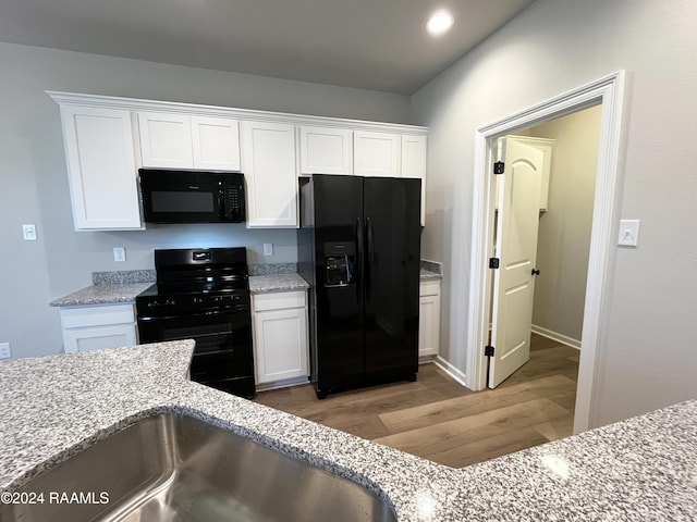 kitchen featuring white cabinets, wood-type flooring, light stone countertops, and black appliances