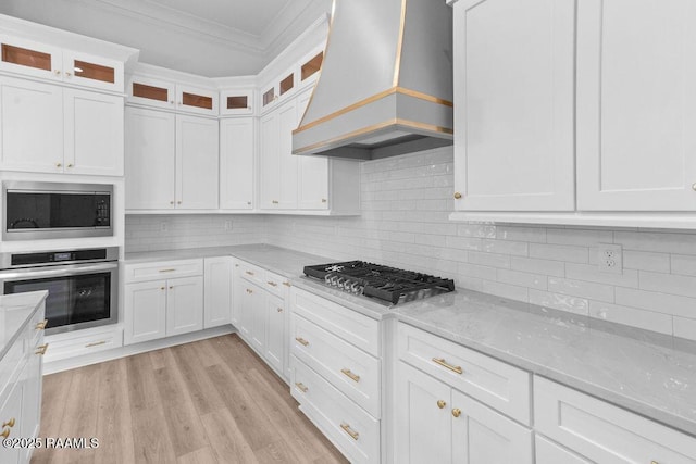 kitchen featuring white cabinets, light wood finished floors, stainless steel appliances, crown molding, and custom range hood