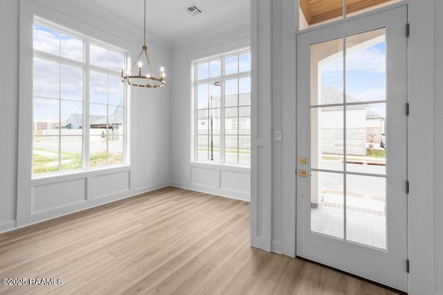 entryway featuring visible vents, an inviting chandelier, light wood-style floors, and a decorative wall