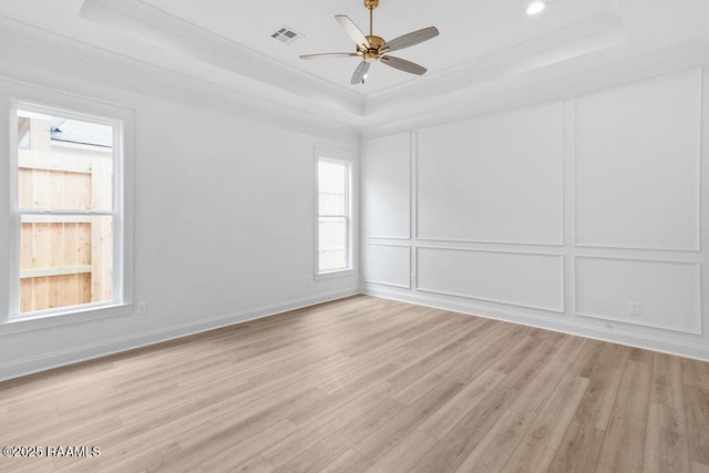 spare room with a decorative wall, light wood-type flooring, ceiling fan, a raised ceiling, and visible vents