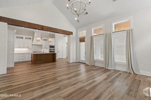 unfurnished living room with sink, a notable chandelier, high vaulted ceiling, and hardwood / wood-style floors