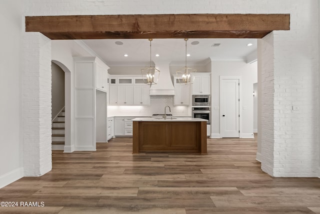 kitchen featuring hardwood / wood-style floors, appliances with stainless steel finishes, a kitchen island with sink, pendant lighting, and white cabinets