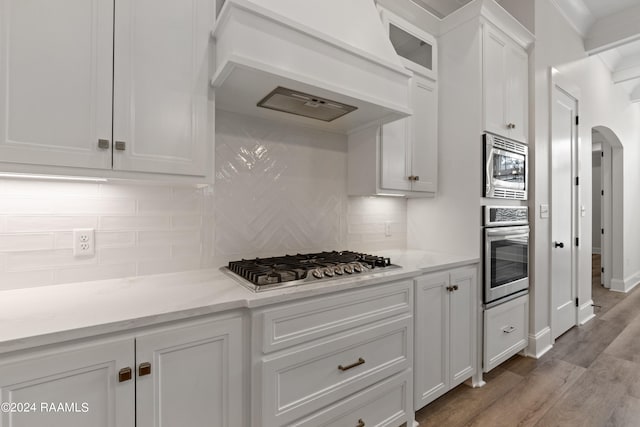 kitchen featuring backsplash, custom range hood, light wood-type flooring, white cabinetry, and stainless steel appliances