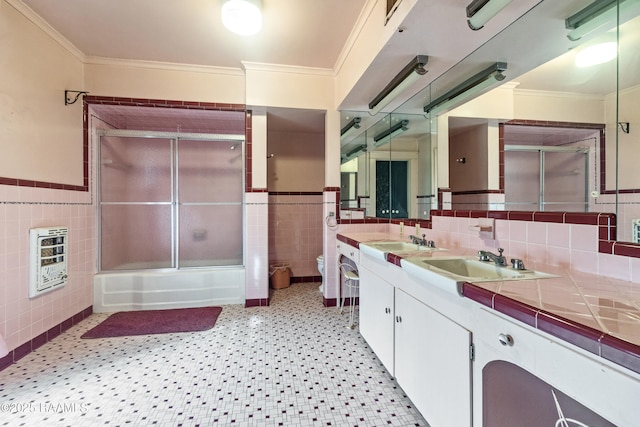 full bathroom featuring toilet, combined bath / shower with glass door, heating unit, tile walls, and ornamental molding