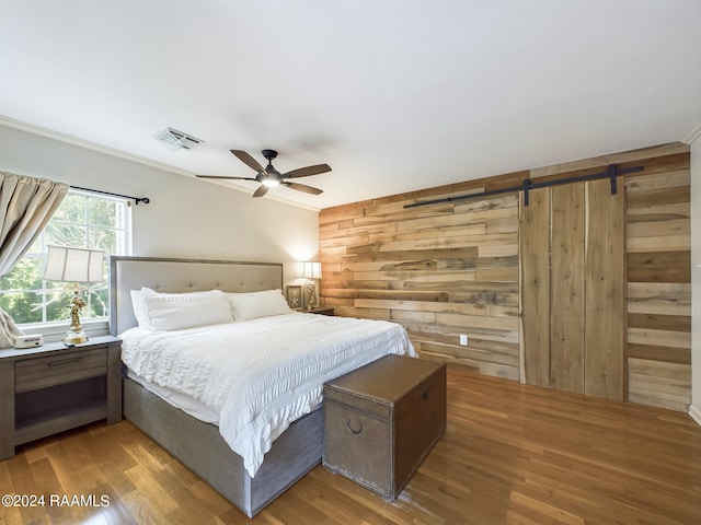 bedroom with wood-type flooring, wooden walls, and a barn door