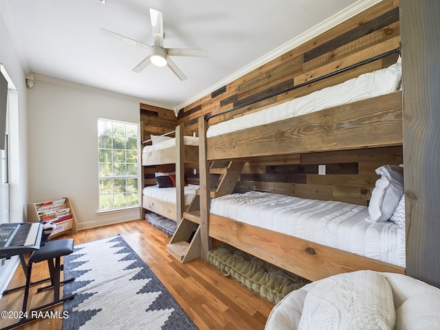 bedroom with ornamental molding, wood walls, ceiling fan, and light hardwood / wood-style floors