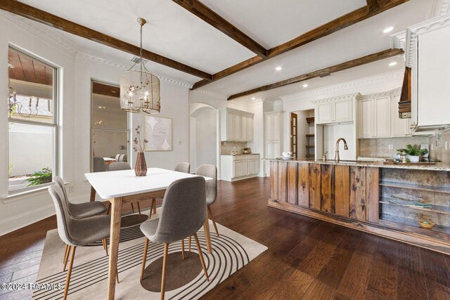 dining room with dark wood-type flooring, an inviting chandelier, beamed ceiling, and sink