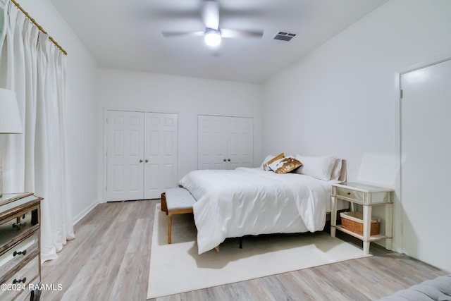 bedroom with light wood-type flooring, ceiling fan, and multiple closets