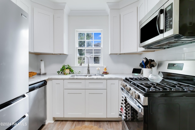 kitchen with appliances with stainless steel finishes, white cabinetry, light hardwood / wood-style flooring, and sink