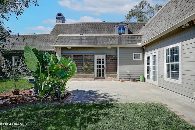 rear view of house featuring a patio, mansard roof, a yard, roof with shingles, and a chimney