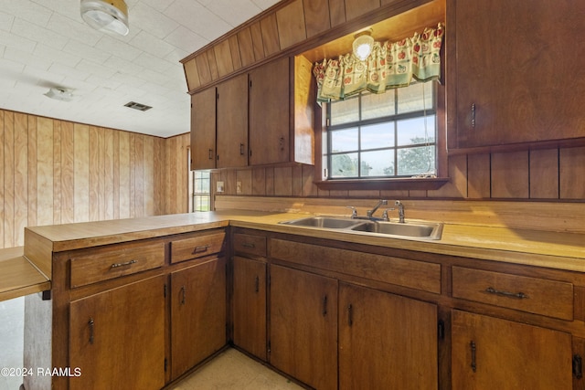 kitchen with wood walls, light tile patterned floors, kitchen peninsula, and sink