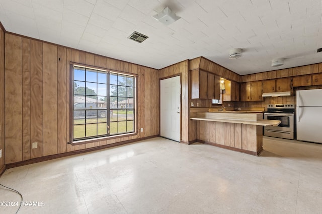 kitchen with a breakfast bar area, kitchen peninsula, stainless steel range with electric stovetop, white refrigerator, and wooden walls