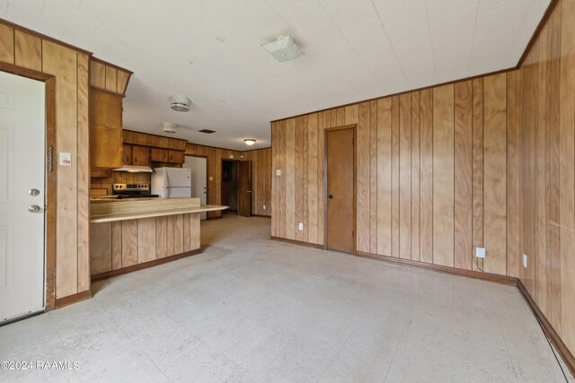 kitchen with stainless steel electric stove, kitchen peninsula, wood walls, and white fridge