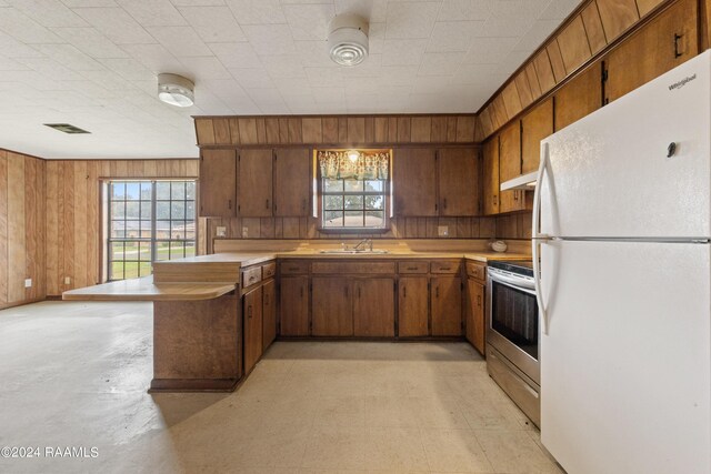 kitchen with white refrigerator, stainless steel electric stove, sink, and wooden walls