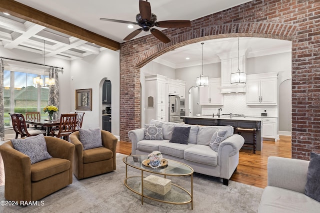 living room with light hardwood / wood-style flooring, ceiling fan with notable chandelier, brick wall, beam ceiling, and ornamental molding