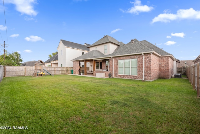 rear view of property featuring a playground, a lawn, a patio, and central AC unit