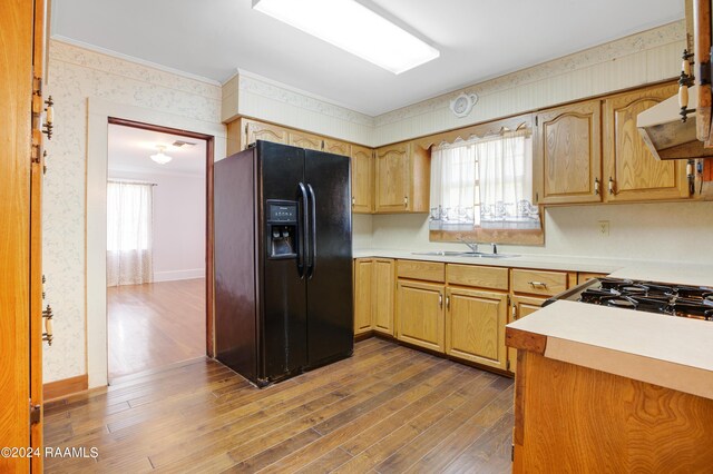 kitchen featuring wood-type flooring, sink, crown molding, and black refrigerator with ice dispenser