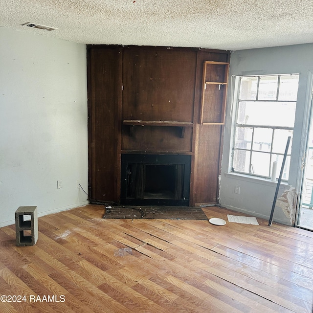 unfurnished living room with hardwood / wood-style floors, a fireplace, visible vents, and a textured ceiling