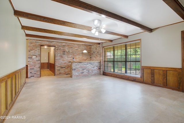 unfurnished living room with beam ceiling, brick wall, ceiling fan, and wainscoting