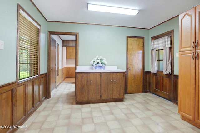 kitchen featuring a wainscoted wall, crown molding, wood walls, and light floors