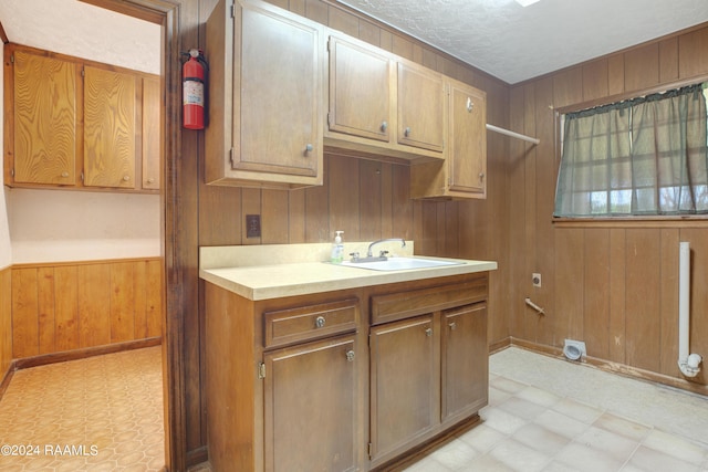 kitchen featuring a textured ceiling, a sink, wooden walls, and light floors