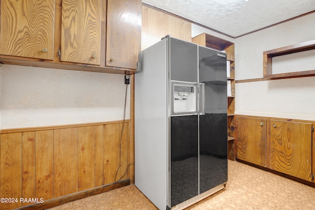 kitchen featuring crown molding, a textured ceiling, wood walls, and fridge with ice dispenser