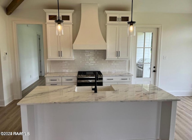 kitchen featuring decorative backsplash, custom exhaust hood, light wood-style flooring, and an island with sink