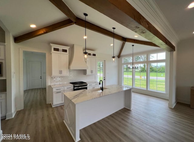 kitchen with an island with sink, gas range, premium range hood, and white cabinetry