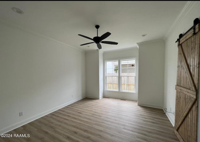 spare room with ornamental molding, hardwood / wood-style floors, ceiling fan, and a barn door