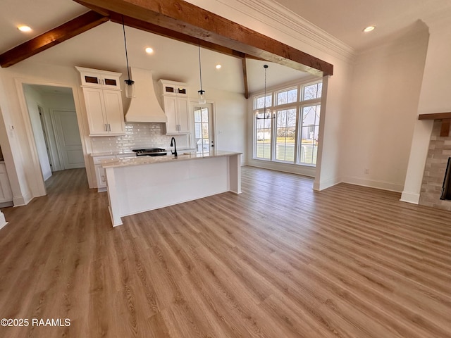 kitchen with a brick fireplace, tasteful backsplash, premium range hood, and light wood finished floors