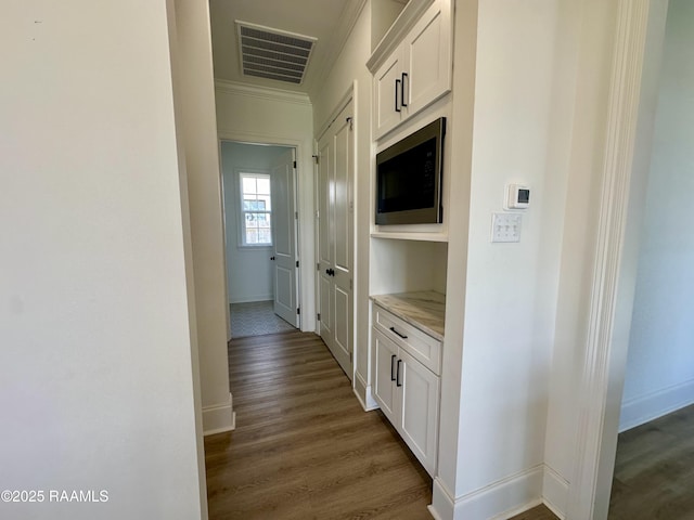 hallway featuring visible vents, baseboards, dark wood-type flooring, and ornamental molding