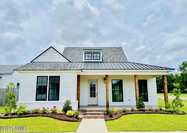 modern farmhouse style home featuring roof with shingles, covered porch, a front yard, and a standing seam roof