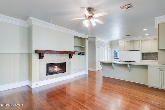 unfurnished living room featuring ceiling fan, light hardwood / wood-style flooring, a tiled fireplace, and crown molding