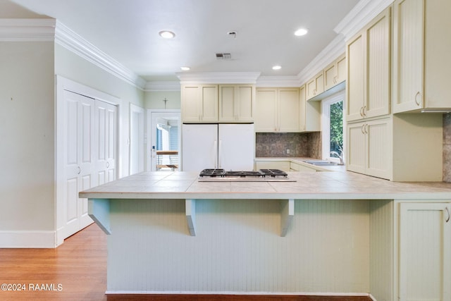 kitchen with white refrigerator, tile countertops, light wood-type flooring, crown molding, and cream cabinets