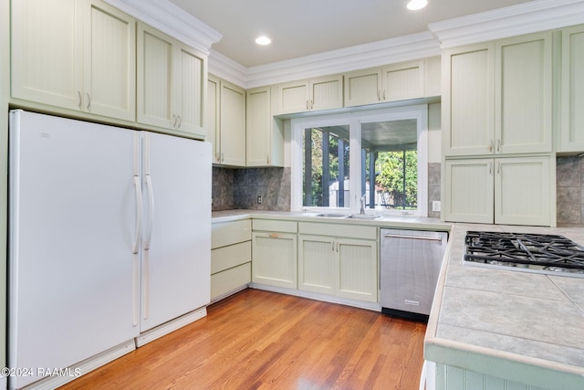 kitchen featuring ornamental molding, stainless steel appliances, tile counters, and light hardwood / wood-style flooring