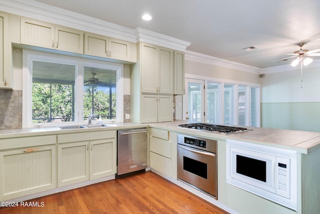 kitchen featuring appliances with stainless steel finishes, cream cabinetry, light hardwood / wood-style floors, and crown molding