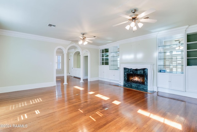 unfurnished living room with ceiling fan, hardwood / wood-style flooring, a premium fireplace, and crown molding