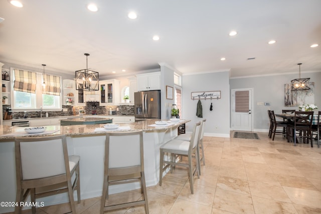 kitchen with crown molding, light stone counters, stainless steel refrigerator with ice dispenser, a breakfast bar area, and decorative backsplash